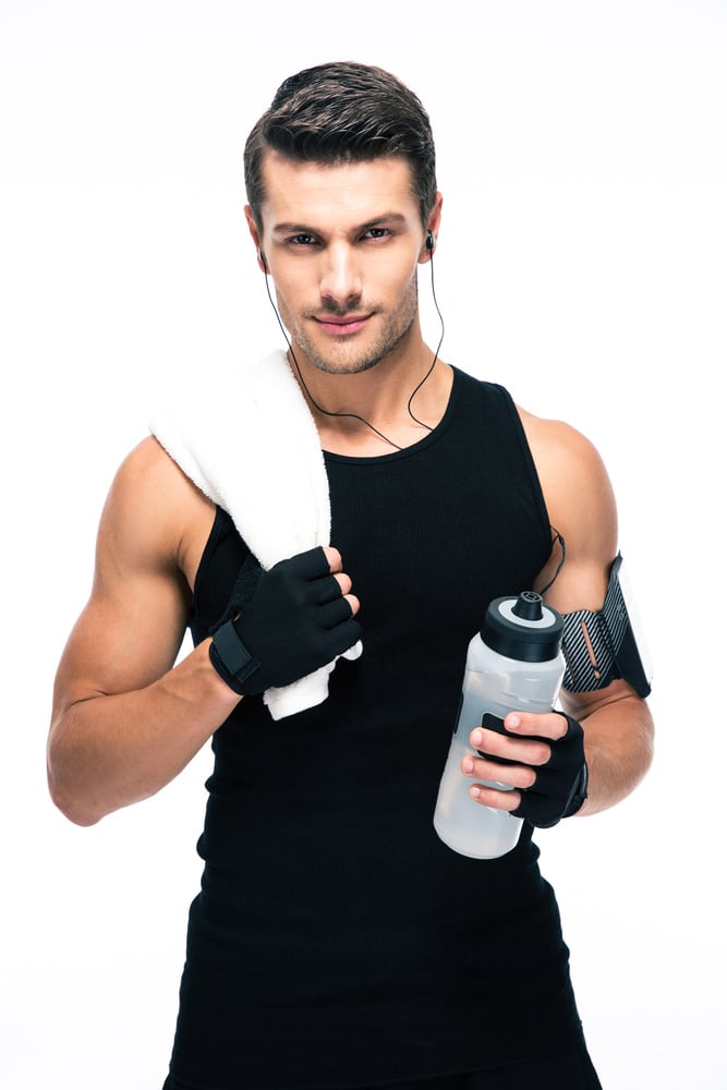 Handsome fitness man holding towel and bottle with water isolated on a white background. Looking at camera